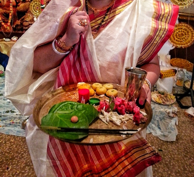 A Bengali lady adorned in traditional red and white sari and holds a puja thali